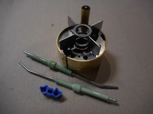 Remeha Brennerkopf mit Elektroden, bestehend aus einem zylindrischen Körper und verschiedenen Stabilisierungselementen. Zubehörteile getrennt angeordnet.